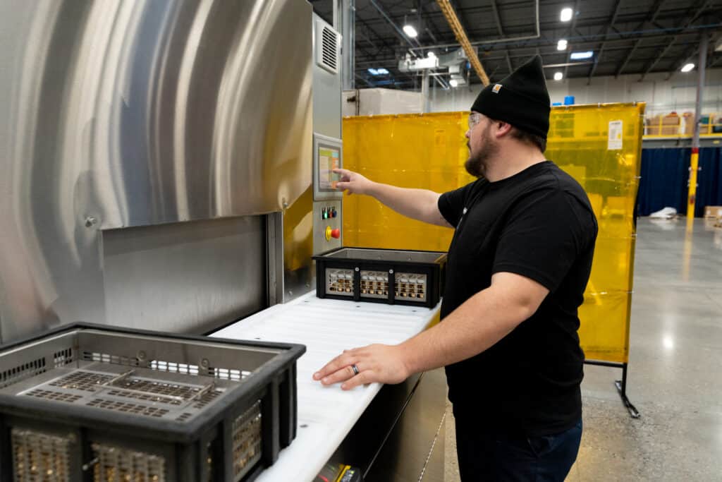 man operating a four basket rotary basket washer to wash industrial parts