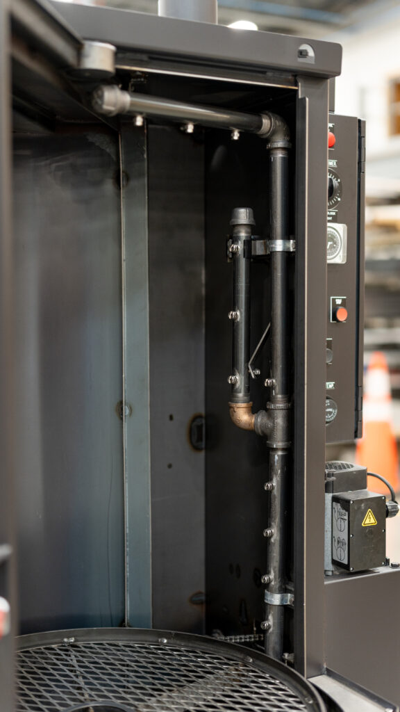 Genesis model industrial parts washer in a factory environment with visible components, control panel, and shop tools.