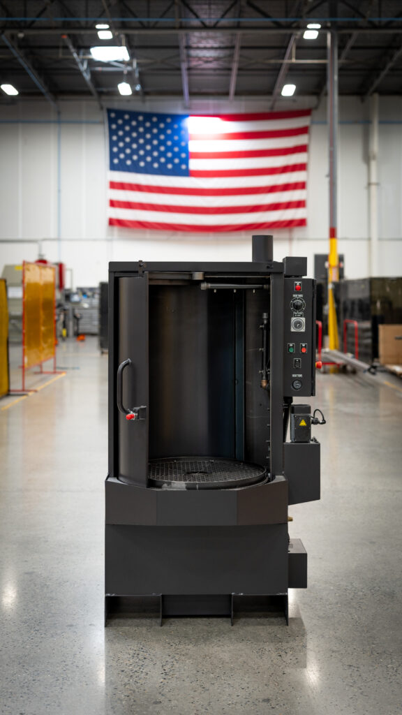 Better Engineering's parts washer displayed in a U.S. manufacturing facility beneath a large American flag.