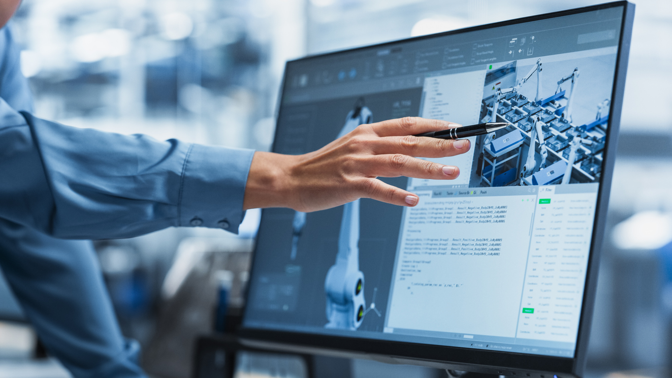 Close-Up On Screen Of Desktop Computer With Automation Software For Autonomous Assembly Line At Modern Factory With Robotic Arms. Technical Supervisor Pointing At Display, Adjusting Production Process